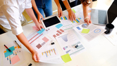 Coworkers discussing data over a table covered with several documents having charts and graphs on them