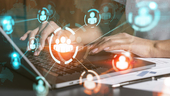 Hands typing at a computer superimposed by icons of people intersecting and connecting.