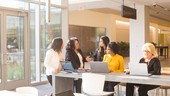 Five Liberty Mutual team members gather at a community table in Liberty Mutual’s common area with laptops, in discussion.