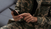 A person in army fatigues holding a cellphone.