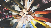 Several people standing in a circle with their hands in the center.