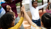Photo of a circle of children holding raised hands and cheering
