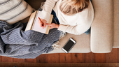 Woman sitting on her couch writing in a notebook.