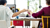 Two co-workers bump their fists together at their desks.