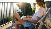 Image of a woman sitting out on a balcony doing work on a laptop as the sun sets