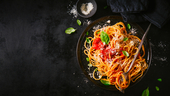 View from above of spaghetti with tomato sauce, parmesan cheese and basil on plate on dark table.