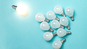 One light bulb outstanding, glowing above a bunch of unlit light bulbs