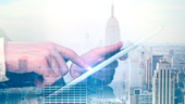 Side view of hand using tablet on New York City background.