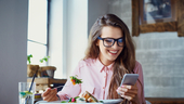 A woman eating a salad and looking at her phone is pictured.