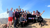 Moov employees hold a flag with the company logo on top of a mountain.