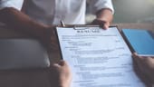 a recent college grad is handing a resume to an interviewer