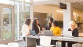 Five Liberty Mutual team members gather at a community table in Liberty Mutual’s common area with laptops, in discussion.