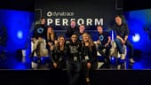 Nine Dynatrace team members sit on a stage with blue backlighting and a sign reading “Dynatrace Perform.”