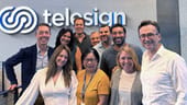 A group of Telesign employees stand together in front of the company sign.