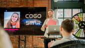 Cogo Labs teammate standing in front of a brick wall and screen presenting to team