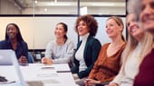 Businesswomen In Modern Office Listening To Presentation By Colleague