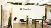 weavegrid's office with its logo on white walls and an open workspace. a man carrying a laptop.