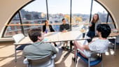 Five people sit around a table in front of a semicircle window