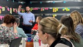 Jon Pinney leads a meeting in front of a wall of Post-It notes.