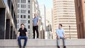 Three NS1 leaders on top of concrete wall amid cityscape background