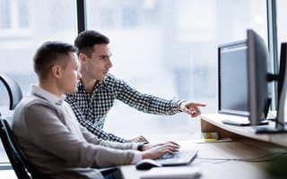 Two advertising professionals sit at a desk looking at a desktop computer screen.