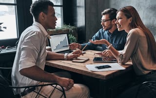 Three people sitting at a desk, talking.