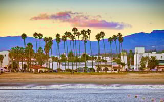 Palm trees on a beach town in the foreground, with a mountainous sunset in the background.