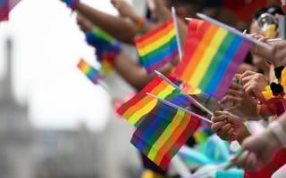 Hands waving Pride flags on the side of a parade