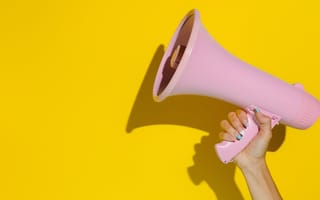 Image of a hand holding up a pink megaphone against a bright yellow background.