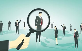 Businessmen standing on top of a globe. A larger hand holding a magnifying glass hovers the glass over one of the men.