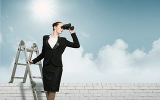 A businesswoman stands on a ladder holding binoculars.
