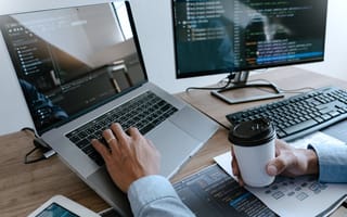 Man works on multiple computer displays while holding coffee cup
