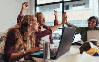 Image of three coworkers celebrating together over their laptops
