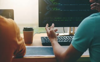 Image of two coworkers discussing the code on computer screens in front of them.