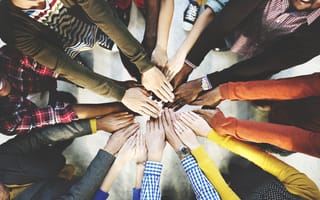 Several people standing in a circle with their hands in the center.