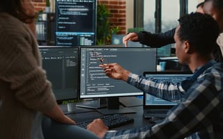 Software developers looking at a monitor discussing source code