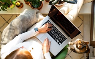 A remote worker with her cat next to her laptop