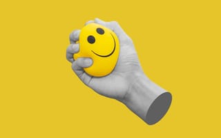 A hand gripping a yellow smiley-face stress ball over a yellow background.