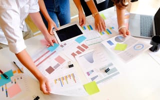 Coworkers discussing data over a table covered with several documents having charts and graphs on them
