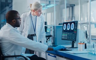Two scientists use computer with screen showing MRI brain scans
