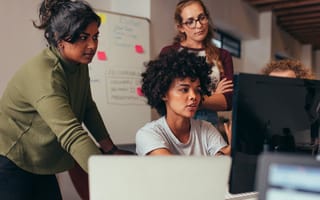 Woman programmer working on computer with colleagues standing behind he looking at her computer monitor