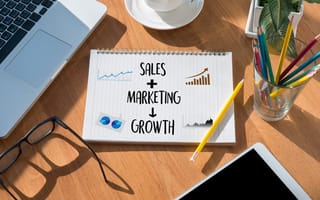 A notebook on a desk with sales + marketing with an arrow pointing to the word growth along with some charts and graphs