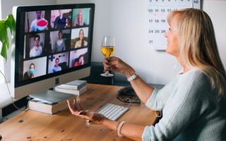 A person drinking wine with their colleagues on a video call.