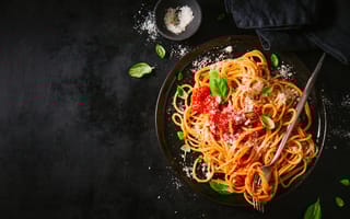 View from above of spaghetti with tomato sauce, parmesan cheese and basil on plate on dark table.