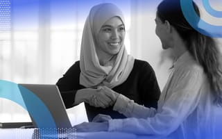 Two women shake hands in front of a laptop computer