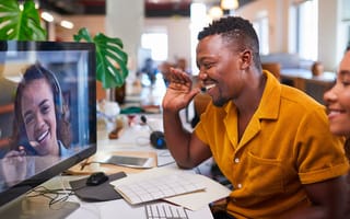 A man waves to his colleague on a video call from his office