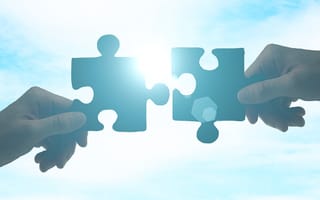 Partnership concept with hands putting puzzle pieces together on sky background with sunlight