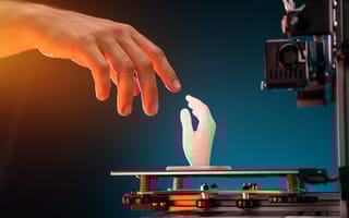 A person's hand reaches out to touch a 3D-printed hand.