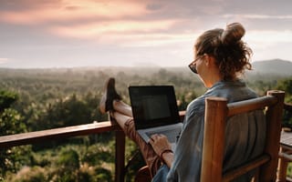 A woman works from a patio overlooking greenery.