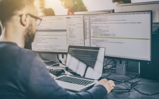 A developer writing code at a desk with three computer monitors.
